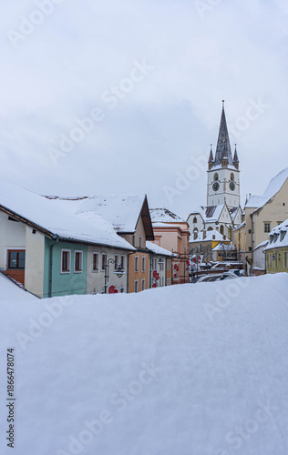 view of frozen downhill street with snow on roofs and main tower on top on cloudy winter day white landscape