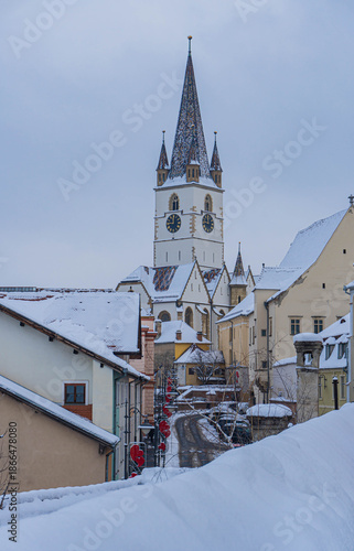 view of frozen downhill street with snow on roofs and main tower on top on cloudy winter day white landscape