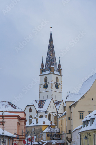 view of frozen downhill street with snow on roofs and main tower on top on cloudy winter day white landscape