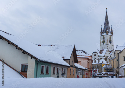 view of frozen downhill street with snow on roofs and main tower on top on cloudy winter day white landscape