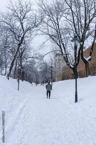old man walking in snowed fairy view of park in winter with trees and medieval tower