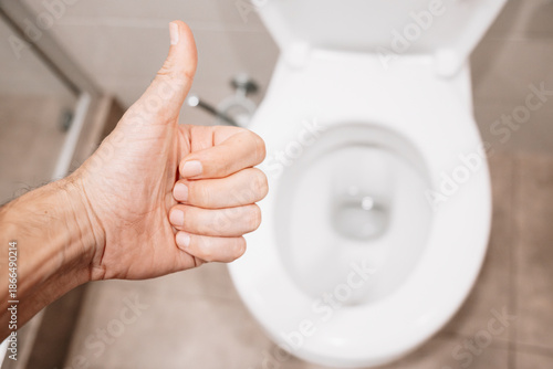 Hand showing thumbs up gesture, indicating satisfaction with the hygiene and cleanliness of a domestic toilet in a bathroom