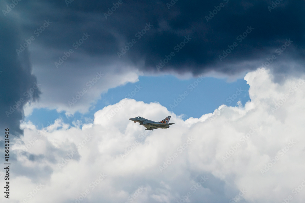 Fototapeta premium Military fighter jet flying through the sky during an aerial demonstration, framed by clouds and open blue space
