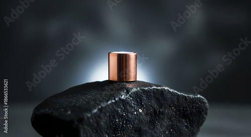 Copper cylinder on black rock with dramatic lighting effect