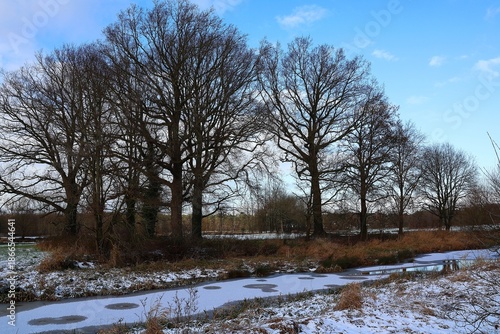 Winter landscape. The slightly frozen 'Kleine Nete' river and a snowy landscape with bare trees in Herentals, Belgium.