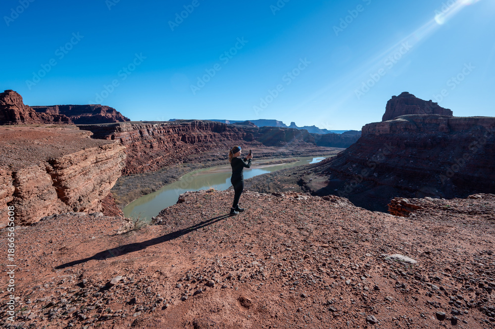 Fototapeta premium Woman photographs Colorado River from overlook on Potash Road near Moab, Utah on clear sunny winter day.