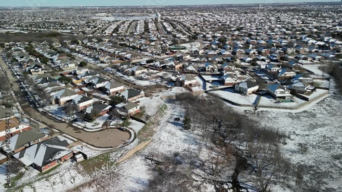 Frisco, Texas, USA - January 3rd, 2024: Drone view of residential suburb with hundreds of snow-covered houses, streets, backyards and distant city skyline under clear winter sky