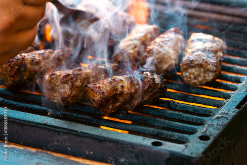 Preparing traditional Romanian meat rolls called mici or mititei on a hot barbecue grill with fire flames