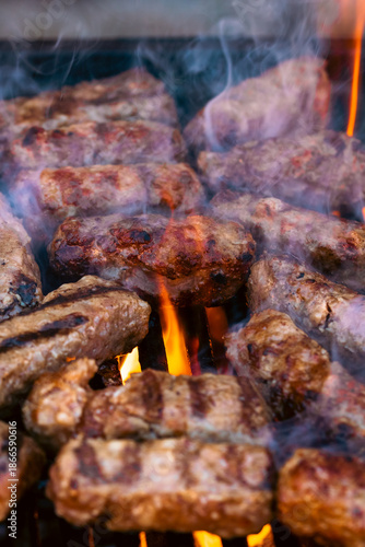 Preparing traditional Romanian meat rolls called mici or mititei on a hot barbecue grill with fire flames