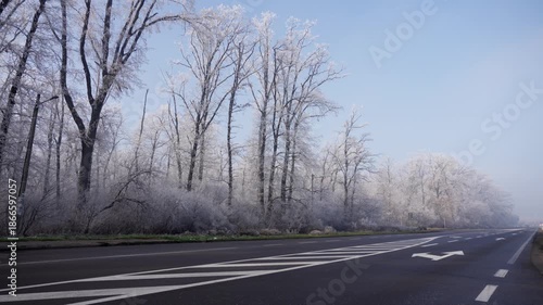 Empty asphalt road and frost covered trees at sunrise with car traffic, 4K