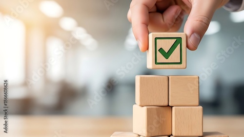 Hand placing final wooden block with green checkmark on stacked cubes