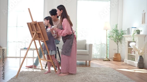 Parents guiding their daughter as she paints on an easel, enjoying a creative family activity together