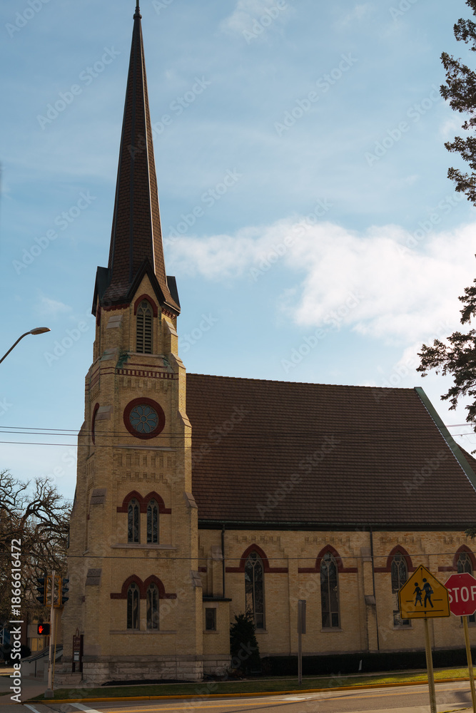 Obraz premium Yellow stone Gothic church in the United States against a clear blue sky. Historic religious architecture, faith and heritage concept