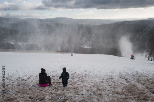 Obraz na plátne Children on a bobsleigh ride downhill past a snow maker