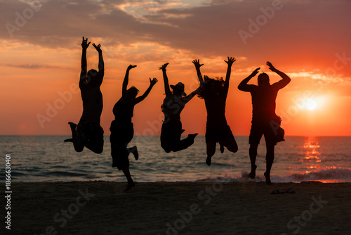 Silhouette of five people jumping with joy on the seashore during a warm and colorful summer sunset at the beach