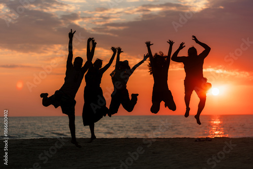 Silhouette of five people jumping with joy on the seashore during a warm and colorful summer sunset at the beach