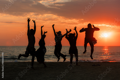 Silhouette of five people jumping with joy on the seashore during a warm and colorful summer sunset at the beach