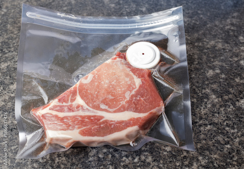 Slika na platnu Pork chop vacuum packed in plastic bag on marble countertop.