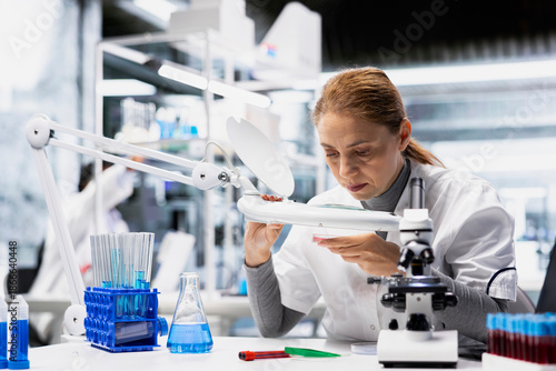 Fotografi Lab technician checking bacterial growth on petri dish under lamp light