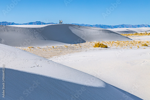 Tiny visitors walk along a high white sand dune ridge, emphasizing scale and vastness at White Sands National Park under a clear blue sky.