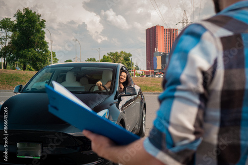 Smiling woman learning to drive and looking out the car window, looking at the instructor with test report. Driving test, driver courses, exam concept
