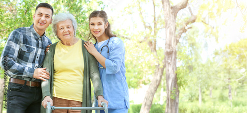 Caregiver and grandson walking with senior woman in park