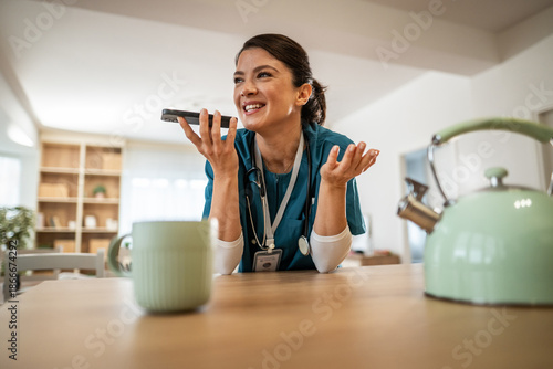Female nurse communicating on phone in a home kitchen