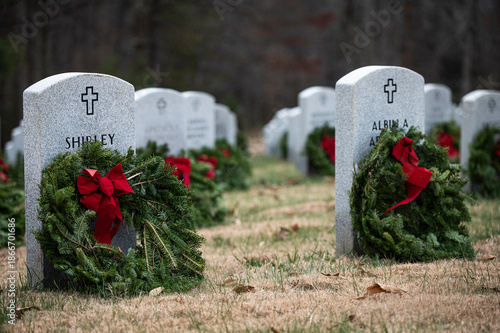 Wreaths with red bows placed on graves at a cemetery by volunteers.