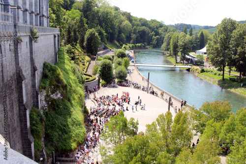 Pilgrims gathering near the side cave / grotto of Our Lady of Lourdes as seen from the basilica, taken in July 2024.