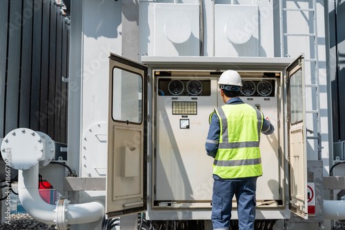 Quadro su tela Professional electrical engineer inspecting control panel and monitoring gauges of power transformer at high voltage substation to ensure energy infrastructure efficiency and safety