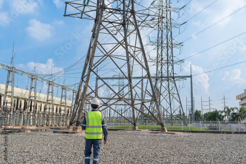 Engineer standing in an outdoor power facility, inspecting transmission structures and overhead lines, supporting grid safety, infrastructure reliability, and preventive maintenance operations.