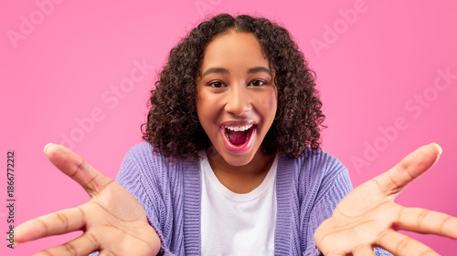 Vászonkép A young person with curly hair smiles widely while extending both hands forward