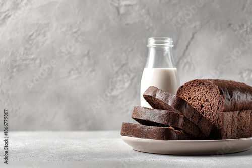 Sliced dark bread on a plate with milk bottle against a textured gray backdrop