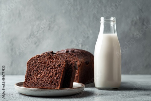 A moist chocolate loaf with a slice, and a bottle of milk. Grey backdrop