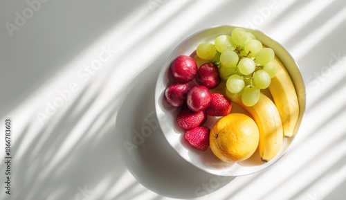 Overhead view of a white bowl filled with assorted fresh fruit, with shadow play