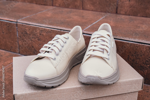 Minimalist eco-friendly white sneakers placed on recycled cardboard box, clean design for sustainable fashion concepts. New unbranded beige sneakers footwear mockups and modern product displays. For