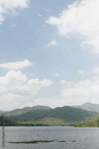 Beautiful outdoor view at Huai Tha Khoei Ban Kha Ratchaburi reservoir. The scene features a wooden photo spot, white ducks, and a calm lake with mountain views.
