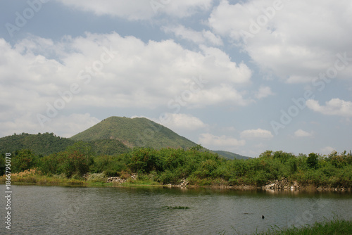 Beautiful outdoor view at Huai Tha Khoei Ban Kha Ratchaburi reservoir. The scene features a wooden photo spot, white ducks, and a calm lake with mountain views.