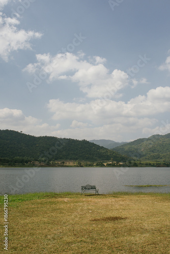 Beautiful outdoor view at Huai Tha Khoei Ban Kha Ratchaburi reservoir. The scene features a wooden photo spot, white ducks, and a calm lake with mountain views.