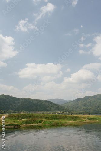 Beautiful outdoor view at Huai Tha Khoei Ban Kha Ratchaburi reservoir. The scene features a wooden photo spot, white ducks, and a calm lake with mountain views.