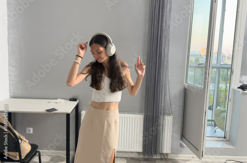 Woman enjoys music and dances inside a room with large windows during sunset