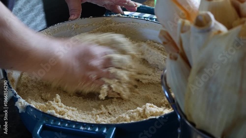 Close-up of a person kneading masa dough in a large bowl to prepare traditional tamales at home