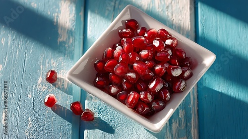 Fresh pomegranate seeds in white bowl on blue wooden table