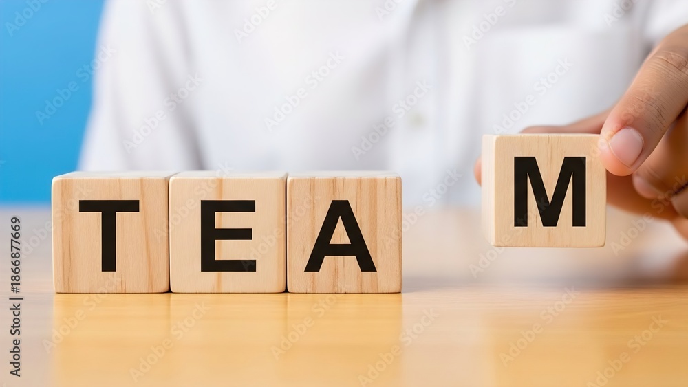 Naklejka premium A hand placing the letter 'M' block to complete the word 'TEAM' spelled out with wooden blocks on a table, symbolizing teamwork and collaboration.
