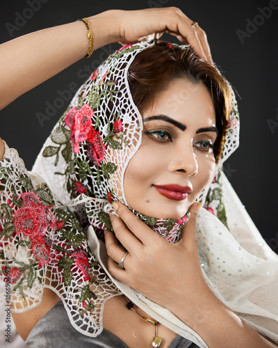 Studio close up portrait of a woman wearing a floral lace scarf, photographed against a dark background with soft lighting.