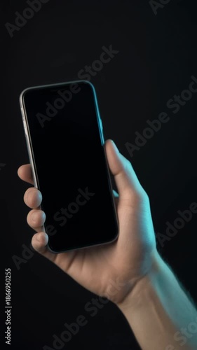 Hand holding a smartphone with a blank screen on a dark background, ready for your content.