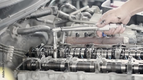 The mechanic is adjusting the valves of a car engine. This image conveys the concentration and dedication of the mechanic working on the engine.