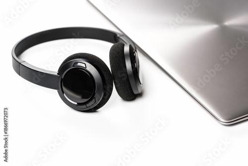 Stylish wireless headphones lying next to closed laptop on minimalist background. Modern work style.