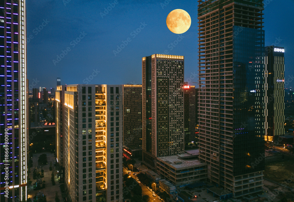 Obraz premium Full Moon Rising Over Illuminated City Skyscrapers at Night