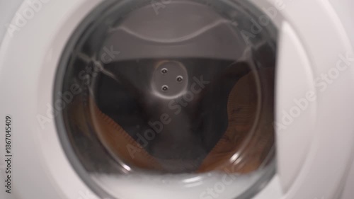 Foamy soap suds churning around shoes in washing machine drum, creating dynamic bubble patterns. Dense white foam envelops footwear during intense cleaning cycle.
